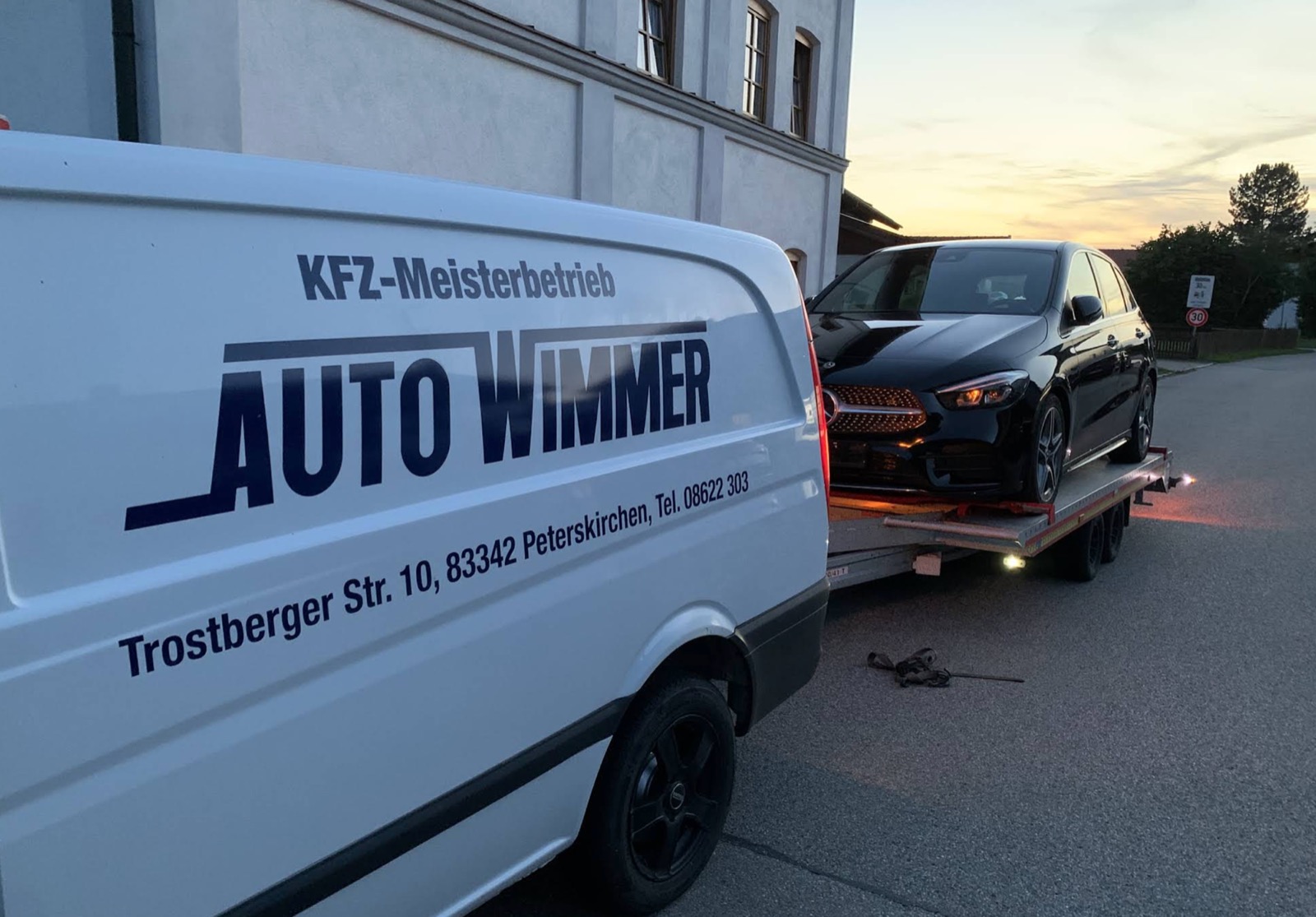 Der beschriftete Transporter von Auto Wimmer mit Autotransportanhänger, darauf ein schwarzer Mercedes